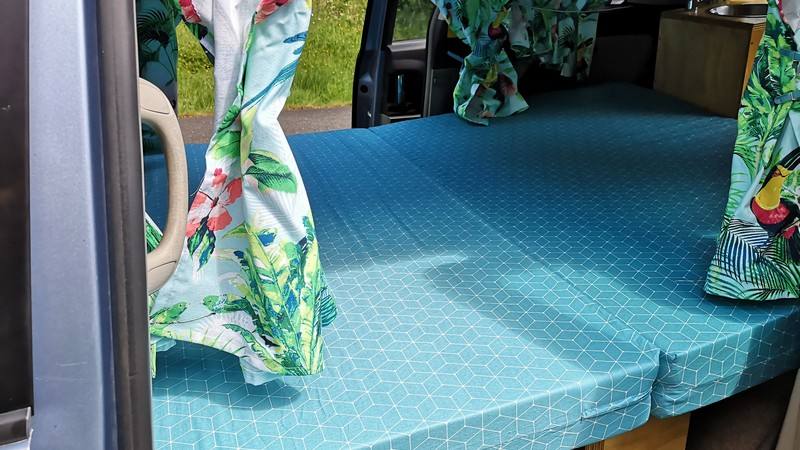 The DJR846 campervan's double bed made up across the van, leaf-print curtains drawn back