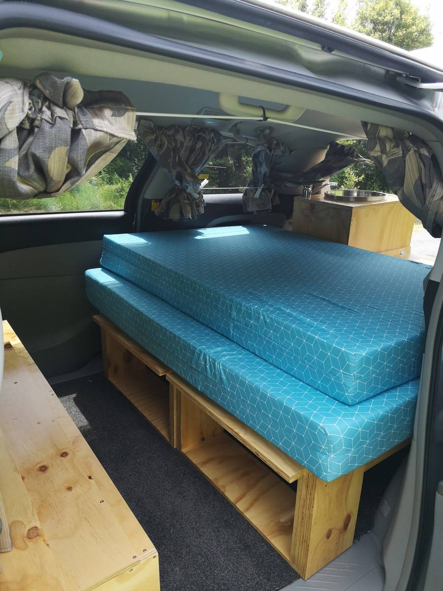 Inside the JTQ214 Toyota Estima campervan, bed on the timber frame with the kitchen unit behind