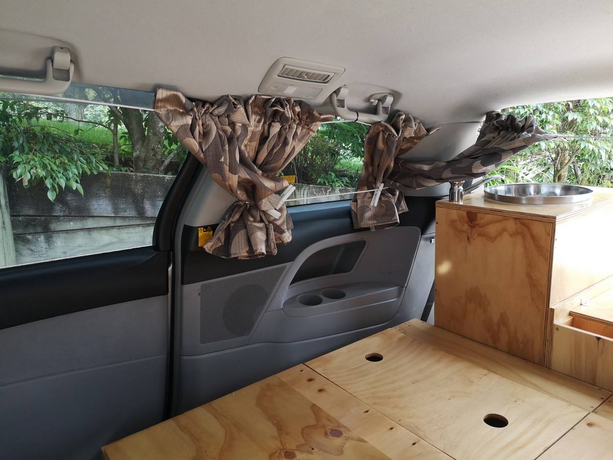 Inside the JTQ214 campervan looking at the side door, curtains and the plywood bed base