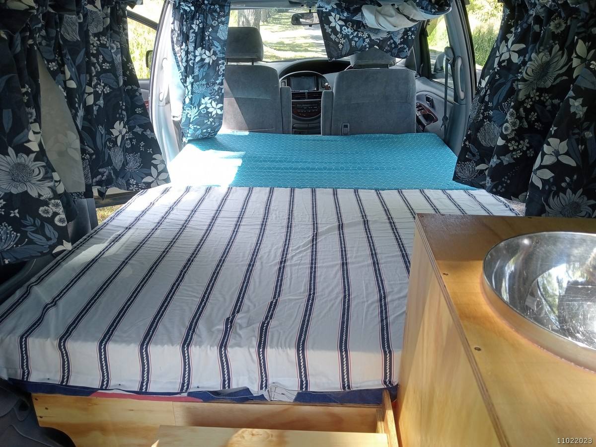 Inside the FDK492 campervan, bed made up beside the sink unit, looking forward to the cab
