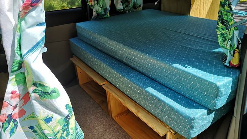 Bed on its plywood base in the DJR846 campervan with storage underneath and leaf-print curtains