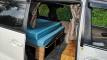 Side door open on the FAC789 campervan, with the double bed made up on its plywood base over the storage drawers