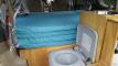 Bed cushions stacked in the JBB773 campervan with the portable toilet out beside the sink unit