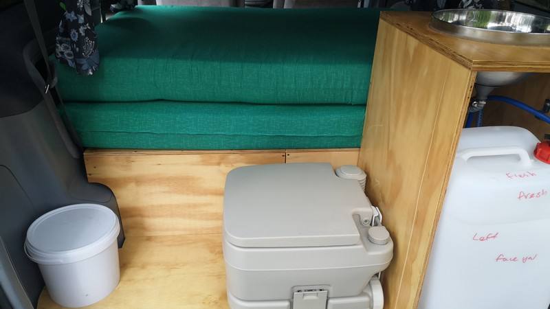 Portable toilet and rubbish bin beside the folded bed cushions in the FDK492 campervan