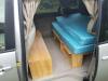 Side door open on the JNQ545 campervan, bed cushions on the timber base with the bench alongside