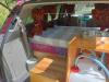 Side door open on the JAK653 campervan, bed made up beside the sink unit and water container