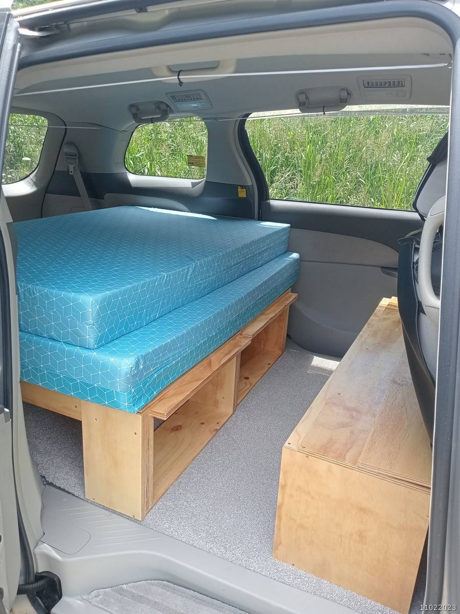 Side door open on the KHP570 campervan, bed on its plywood base with open storage underneath