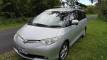 Front three-quarter view of the silver HMC107 Toyota Estima campervan with its roof rack and awning