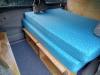 Bed on its plywood base in the GRH325 campervan, with open storage shelves underneath