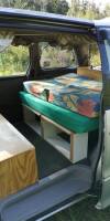Side door open on the GBB26 campervan, bed made up over the open storage shelves with a step below