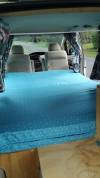 Inside the JBB773 campervan looking forward over the made-up bed to the front seats, floral curtains drawn back