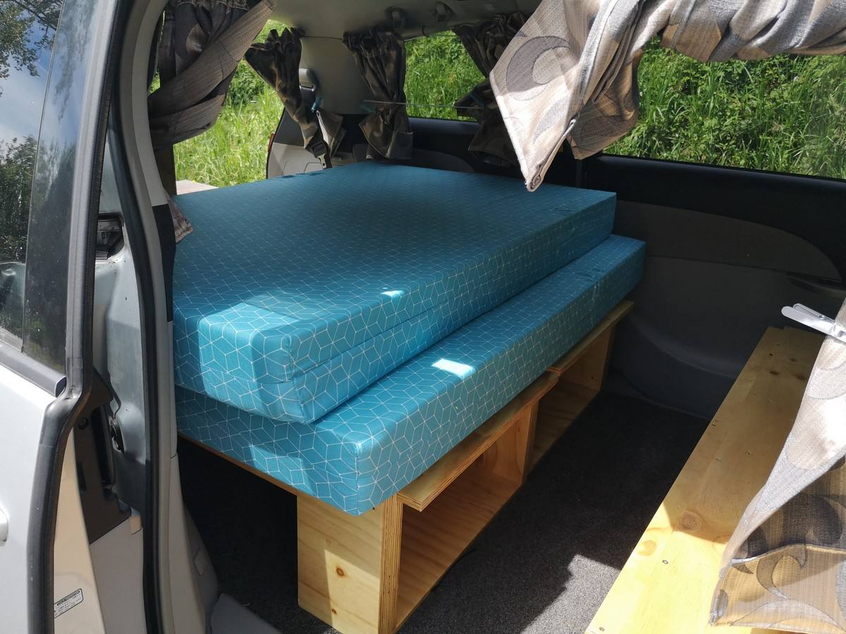 Side door open on the JTQ214 campervan, double bed on its timber frame with a bench seat alongside