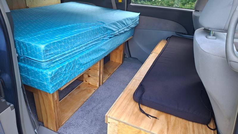 Inside the EYC409 campervan, bed cushion on its timber frame with the bench seat opposite