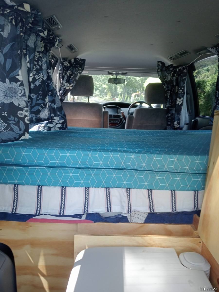 Inside the FDK492 campervan looking forward over the made-up bed, portable toilet stowed below