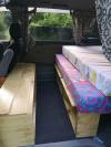 Bed on its plywood base in the FPS382 campervan, with storage below and a bench alongside