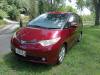Front three-quarter view of the red JAK653 Toyota Estima campervan on a tree-lined drive
