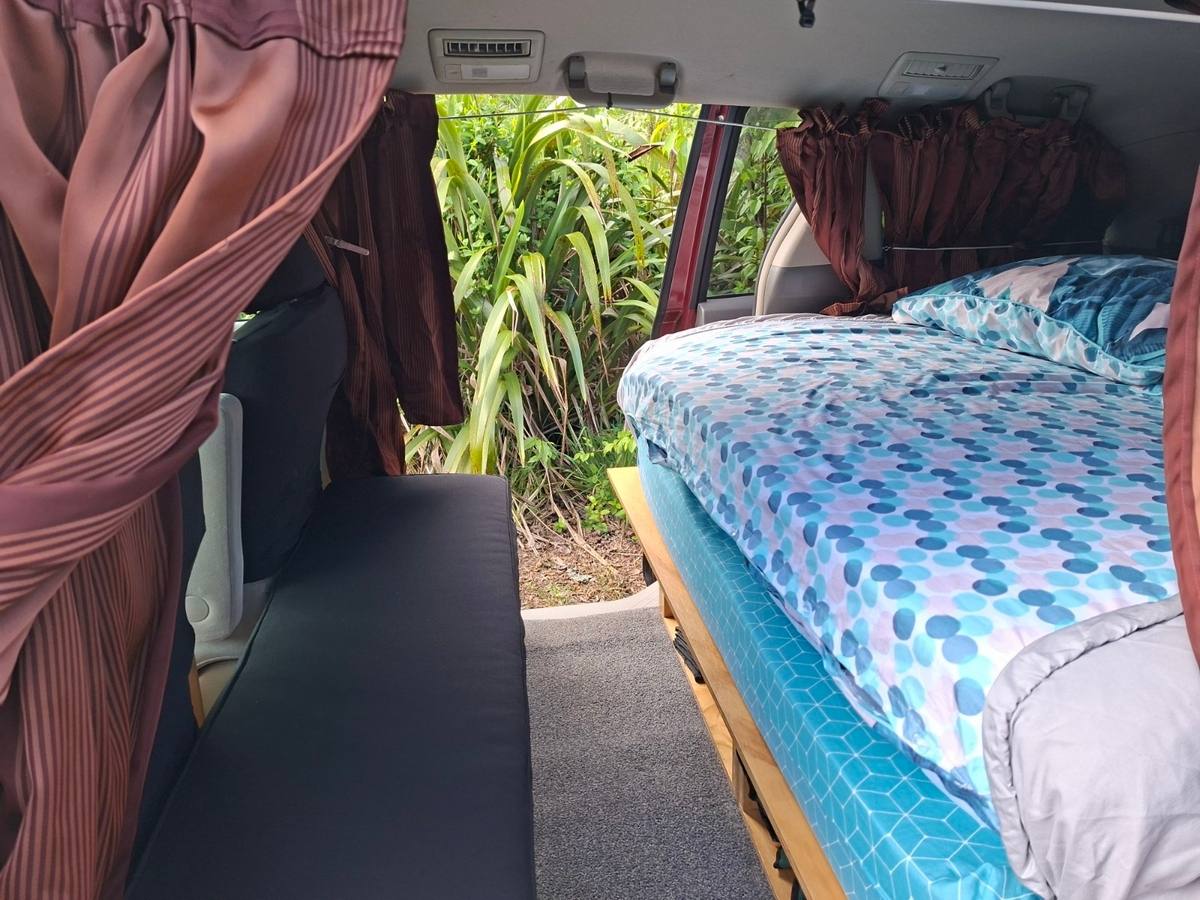 Inside the JAK653 campervan, bed made up alongside the bench seat, side door open to the greenery