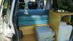 Inside the FYC899 campervan, bed cushions stacked beside the portable toilet and the sink unit