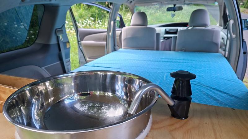 Stainless sink and hand pump tap in the EYC409 campervan, with the made-up bed behind
