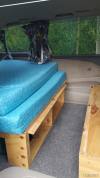 Bed on its plywood base in the JBB773 campervan, with open storage shelves underneath