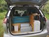 Tailgate open on the JNQ545 campervan parked on a grass verge, kitchen unit and water container inside