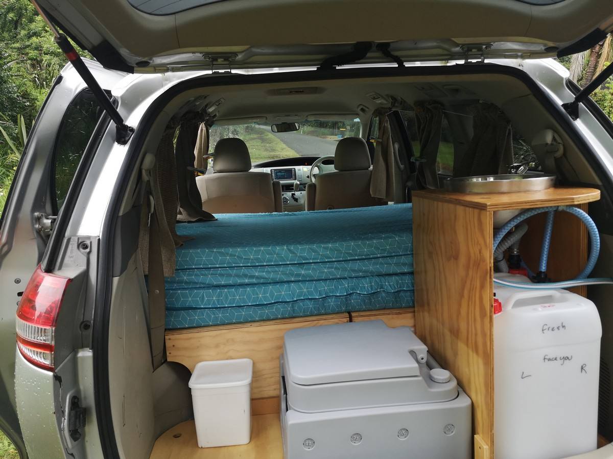 Tailgate open on the JNQ545 campervan, showing the bed, portable toilet, sink unit and water container