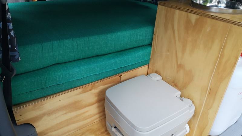 Bed cushions stacked in the FDK492 campervan beside the portable toilet and the plywood kitchen unit