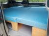 The KHP570 campervan's double bed made up across the van, storage boxes underneath