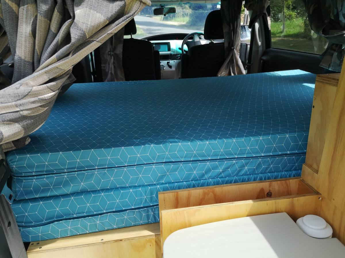 Inside the JTQ214 campervan looking forward over the made-up bed, portable toilet stowed alongside
