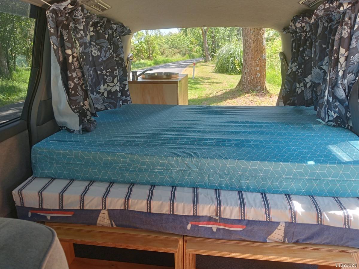 The FDK492 campervan's double bed made up, looking out through the open tailgate