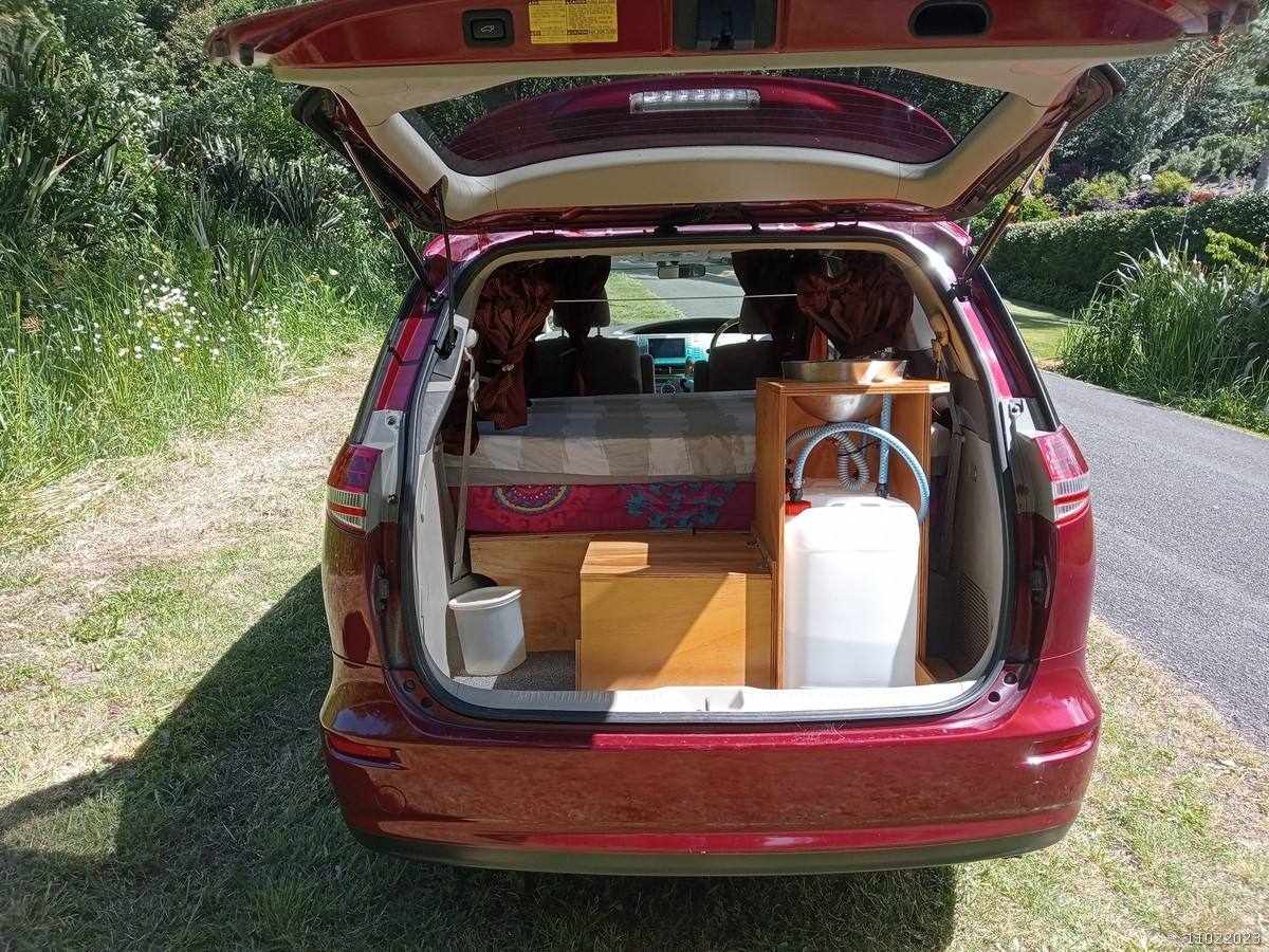 Tailgate open on the red JAK653 campervan, showing the bed, kitchen unit and fresh water container