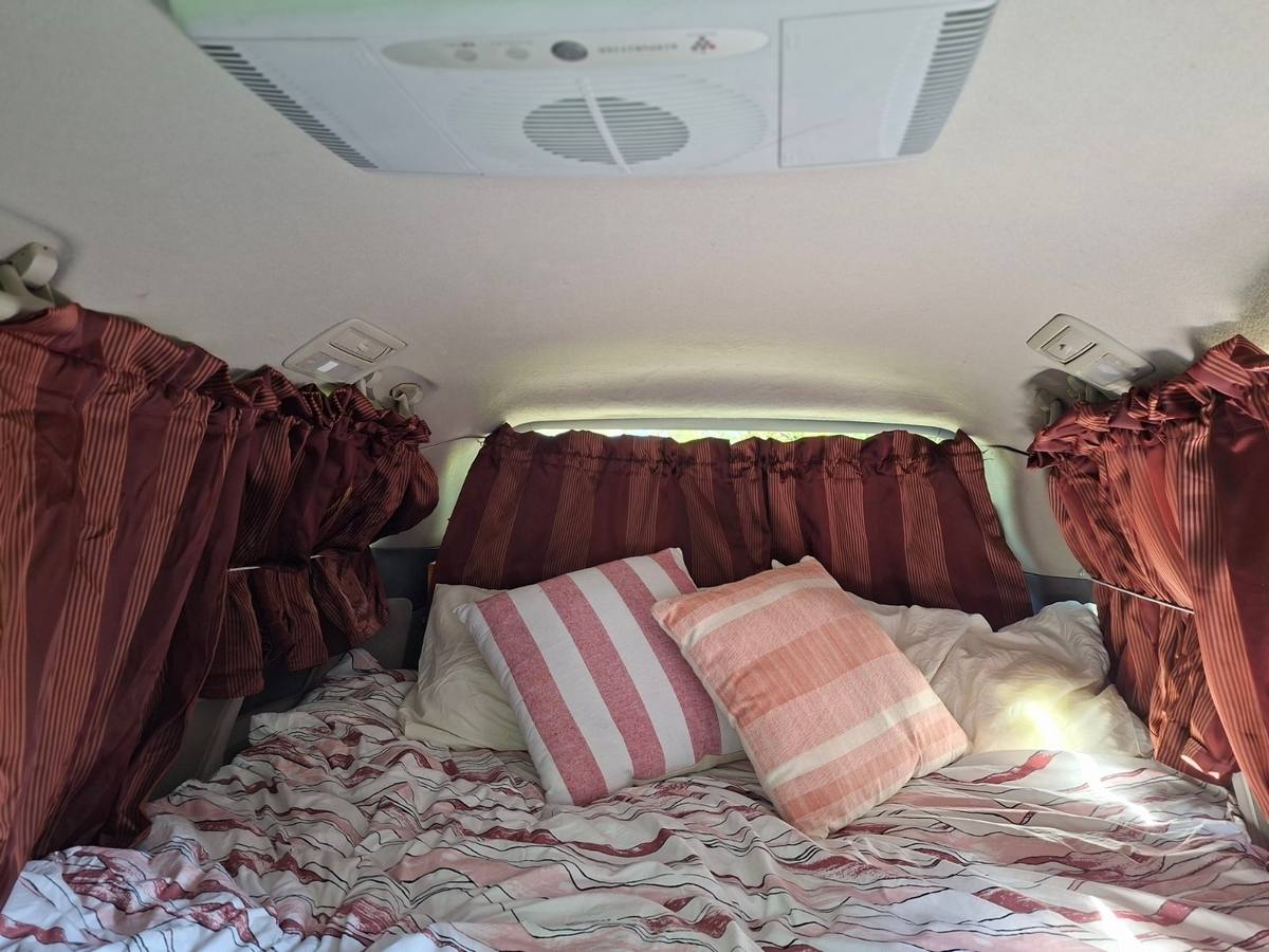 Bed made up with pillows in the back of the JAK653 campervan, roof vent above