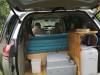 Tailgate open on the JNQ545 campervan, showing the bed, portable toilet, sink unit and water container