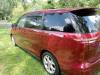 Rear three-quarter view of the red 2006 Toyota Estima campervan JAK653 parked on grass