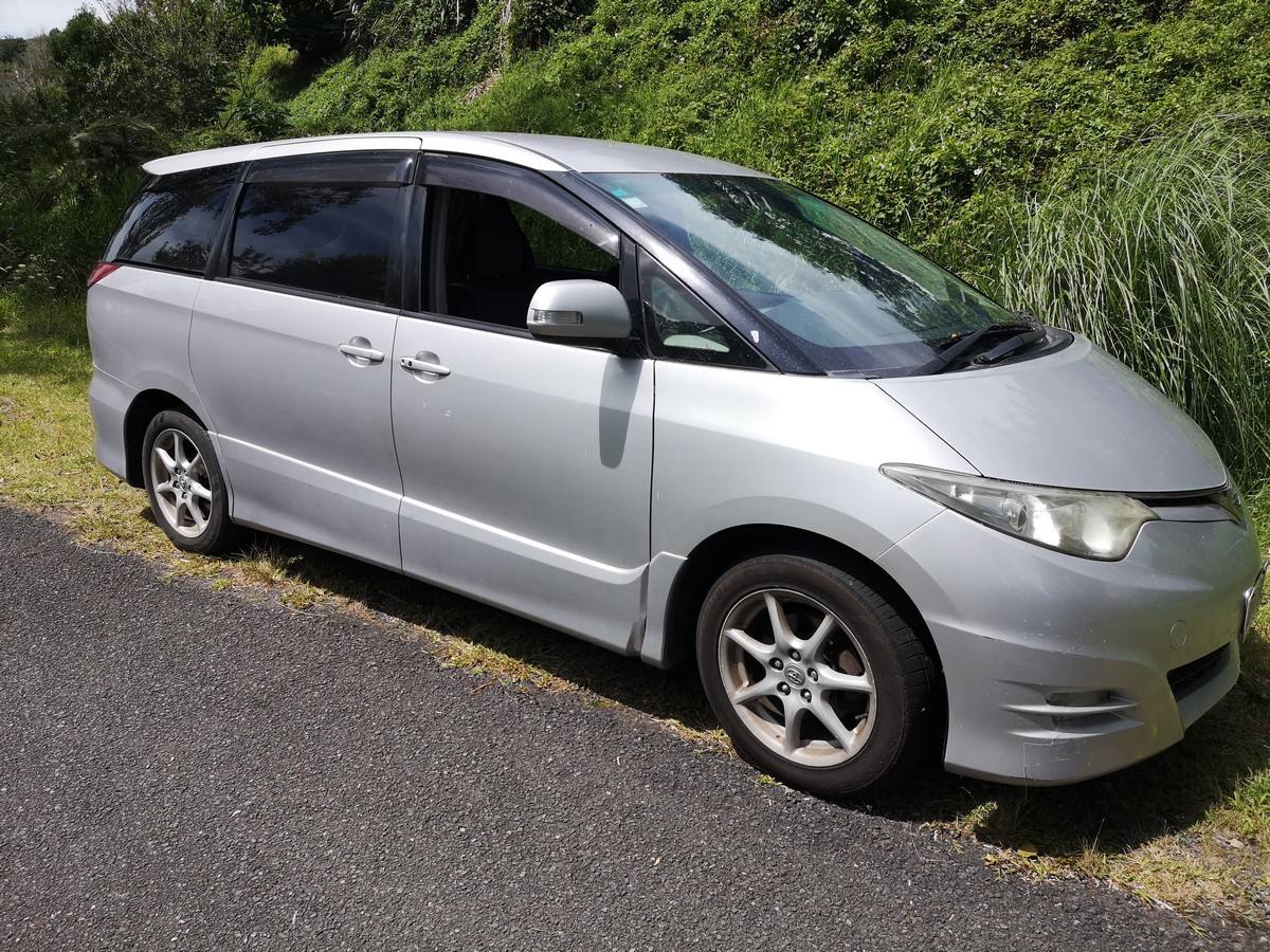 Front three-quarter view of the silver 2007 Toyota Estima campervan JTQ214 on a country road